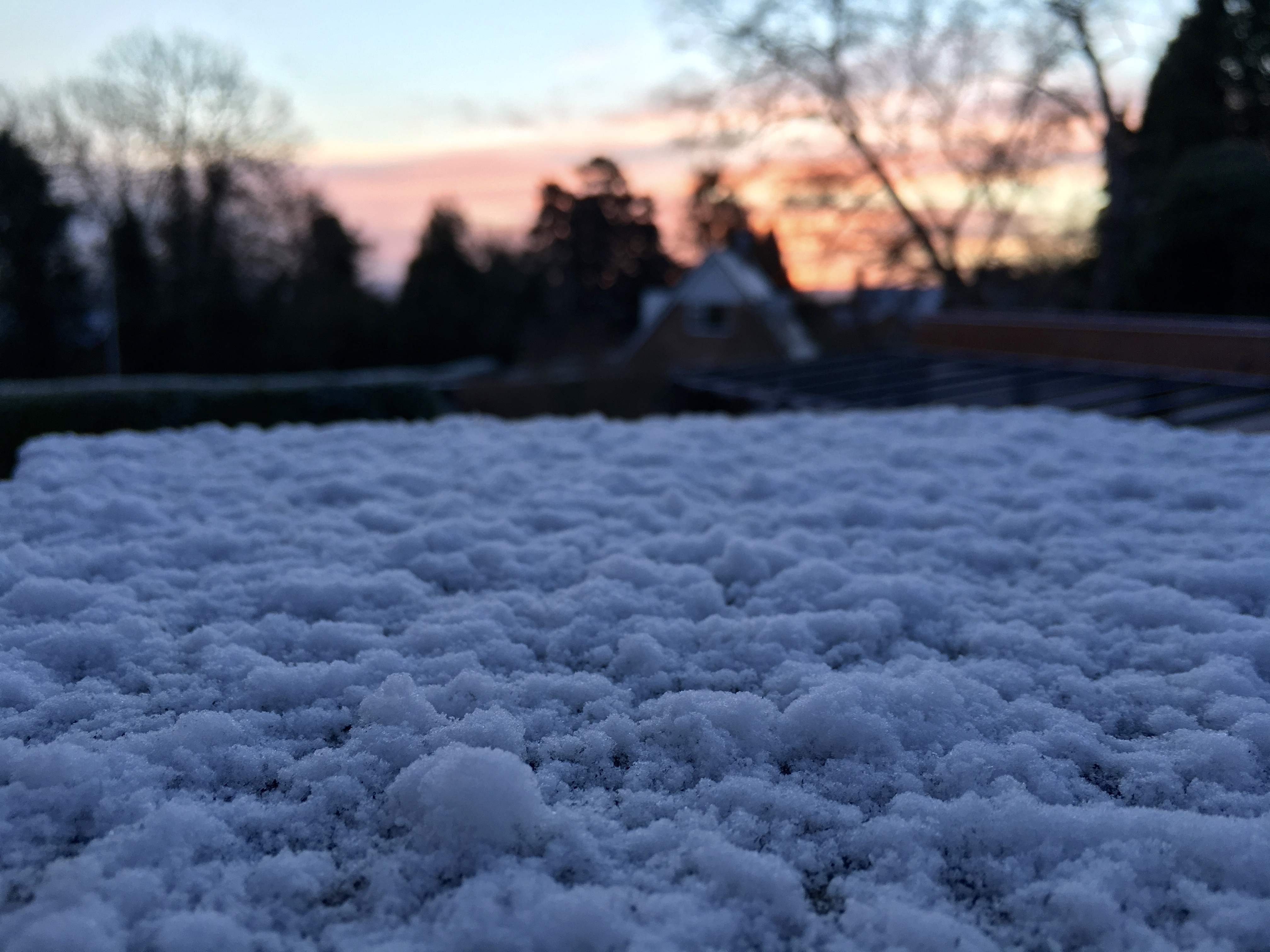 Close up picture of snow with a pink and orange sunrise in the background.