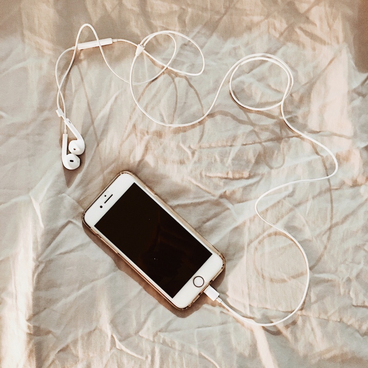 iPhone with headphones laying on a grey sheet.