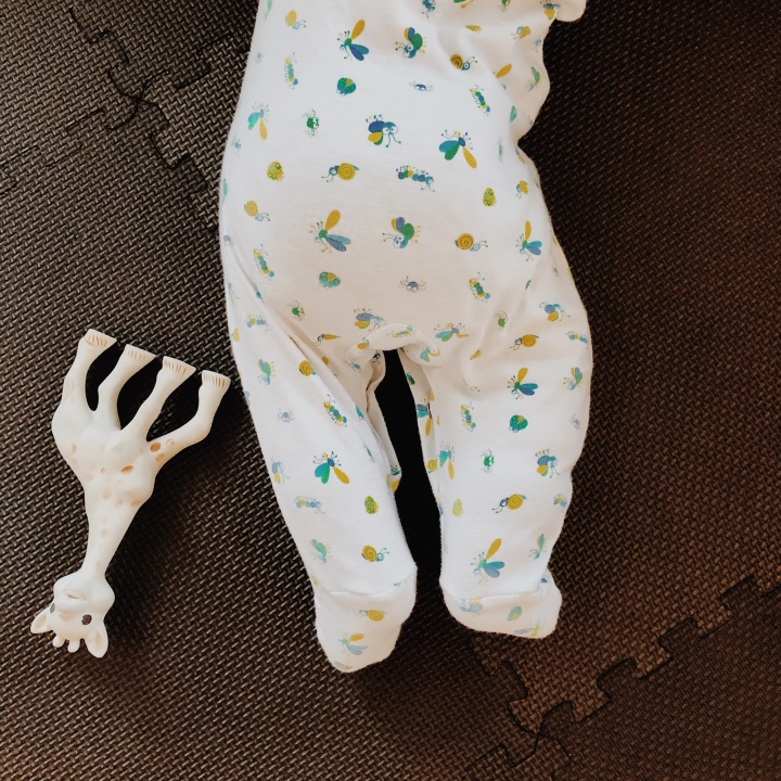 Bottom half of a baby in a romper, beside a Sophie the Giraffe toy.