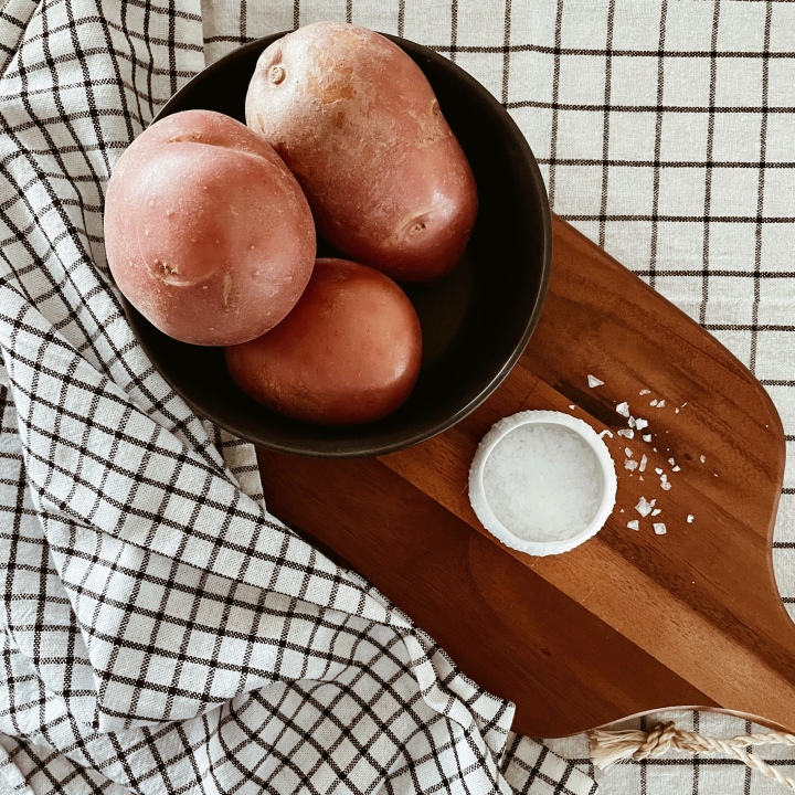 Red potatoes in a bowl on a wooden board besides a salt dish, surrounded by checked cotton tea towels.